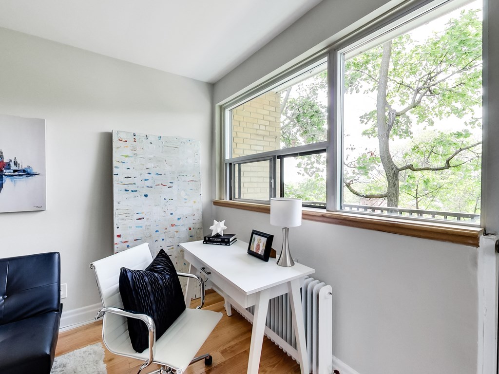 A white desk with a black chair and a white lamp sits in front of a window.