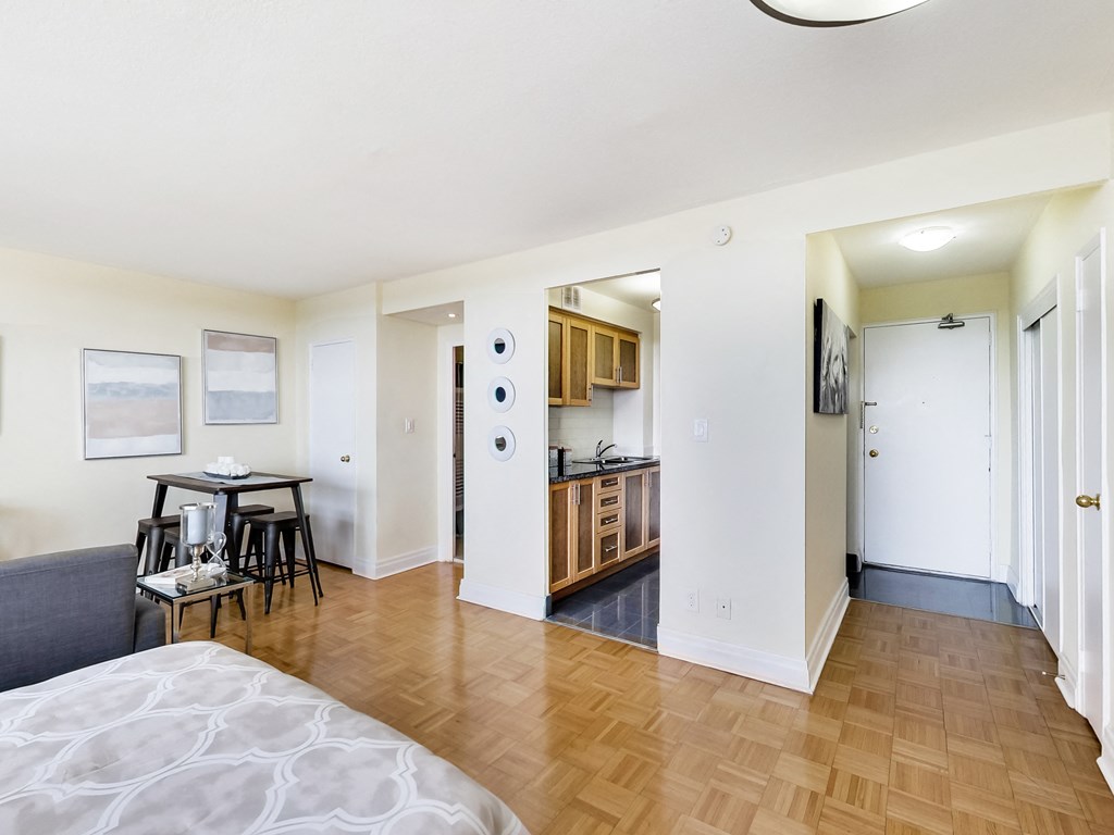 A bedroom with a bed, a table and chairs, and a kitchen area.