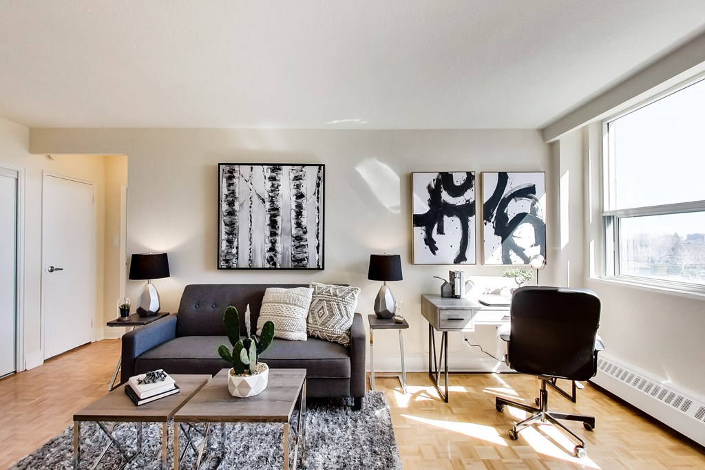 A living room with a grey couch, a black chair, a coffee table, and a painting on the wall.