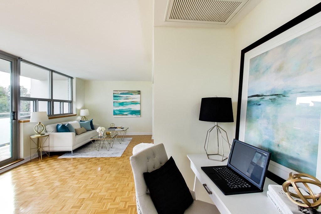 A laptop is on a desk with a lamp and a painting in the background.