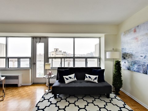 A black couch with white pillows sits in a living room with a large window.