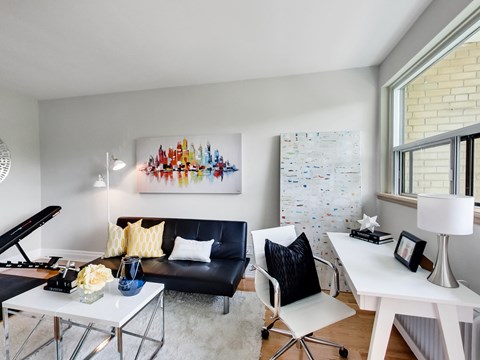 A modern living room with a black couch, a white coffee table, and a colorful abstract painting on the wall.