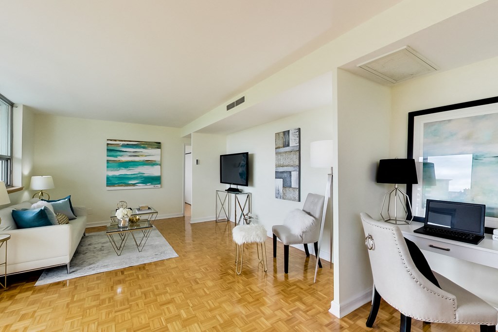 A living room with a white couch, a television, a chair, and a desk with a laptop.