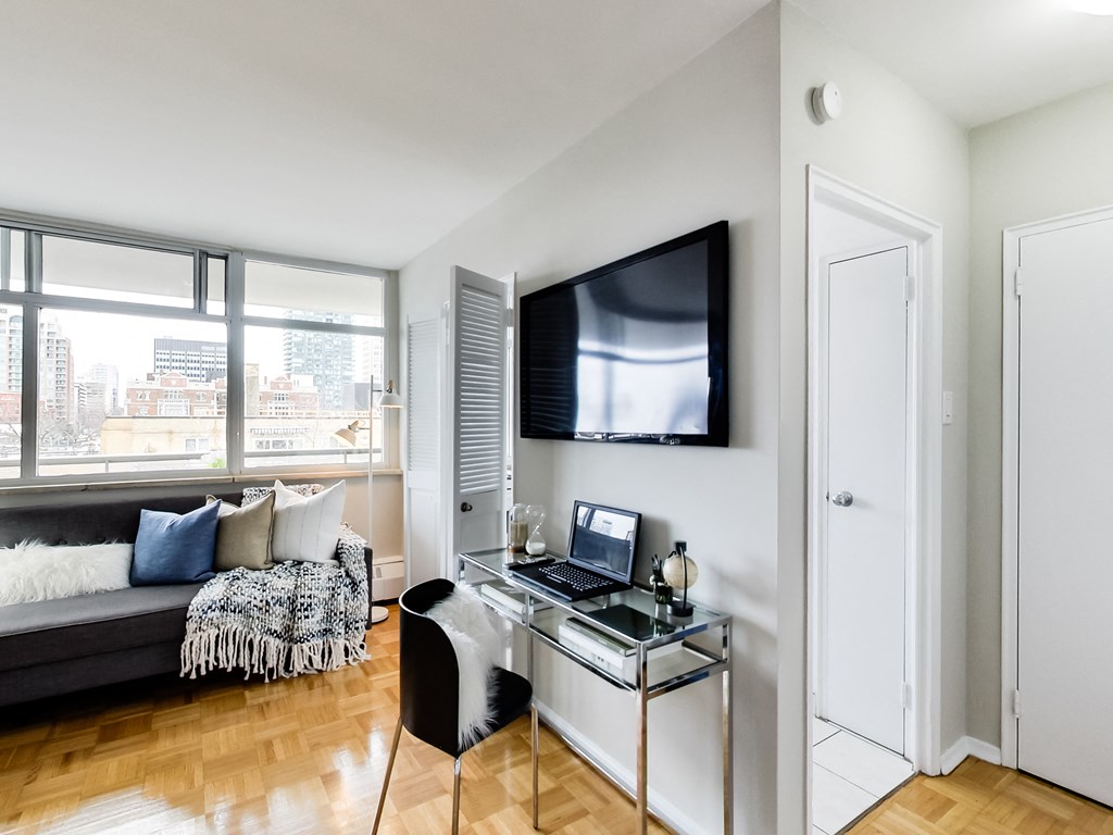 A modern living room with a black couch, a glass coffee table, and a television mounted on the wall.