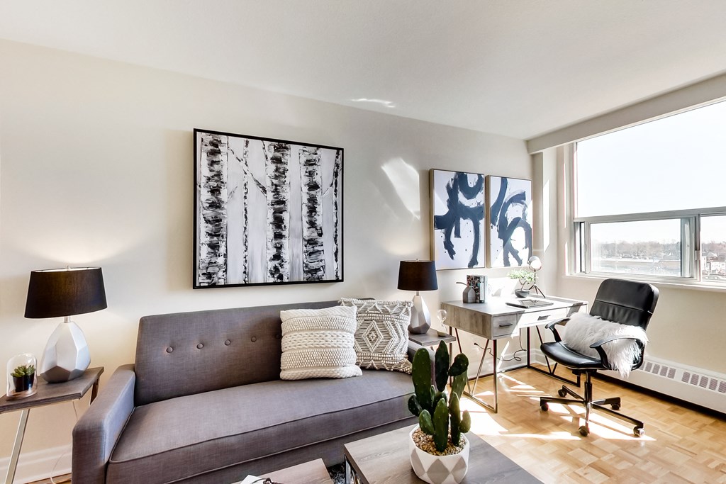 A living room with a grey couch, a table with a chair, and a painting on the wall.