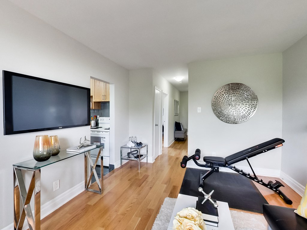 A black TV is mounted on a white wall above a glass table with a vase on it.