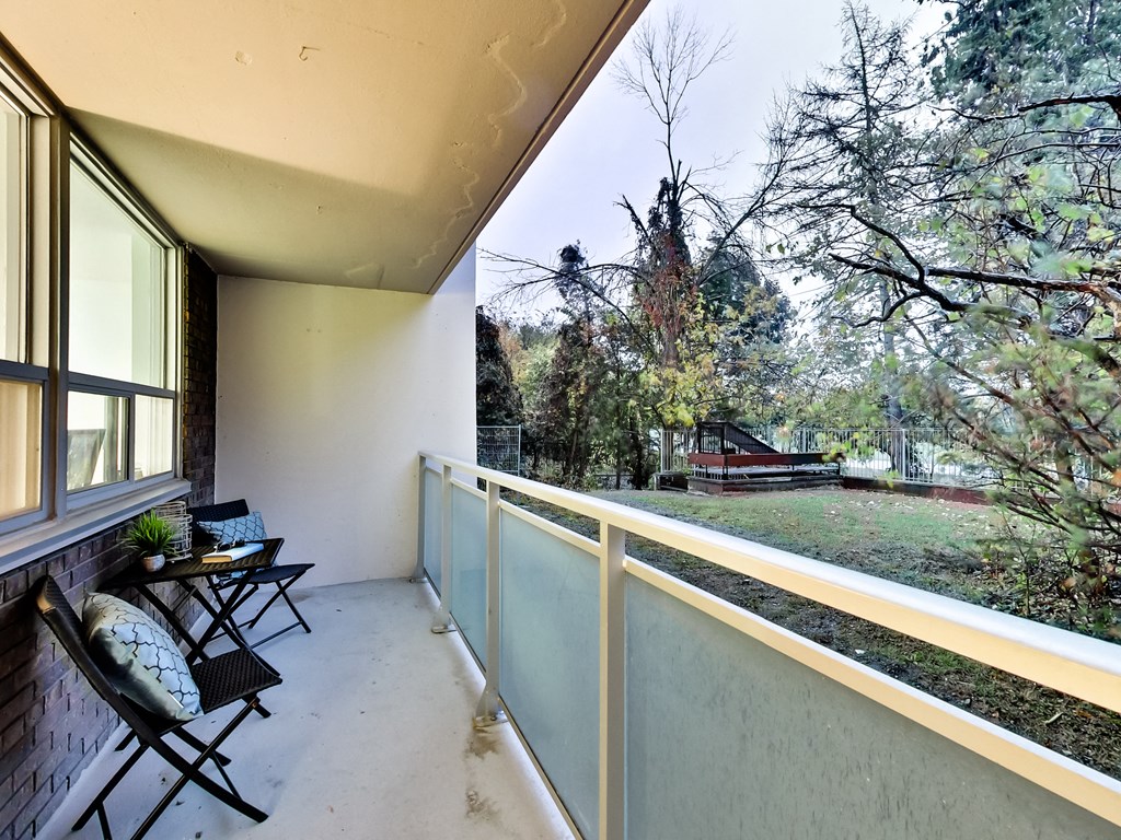 A balcony with chairs and a table overlooking a backyard.