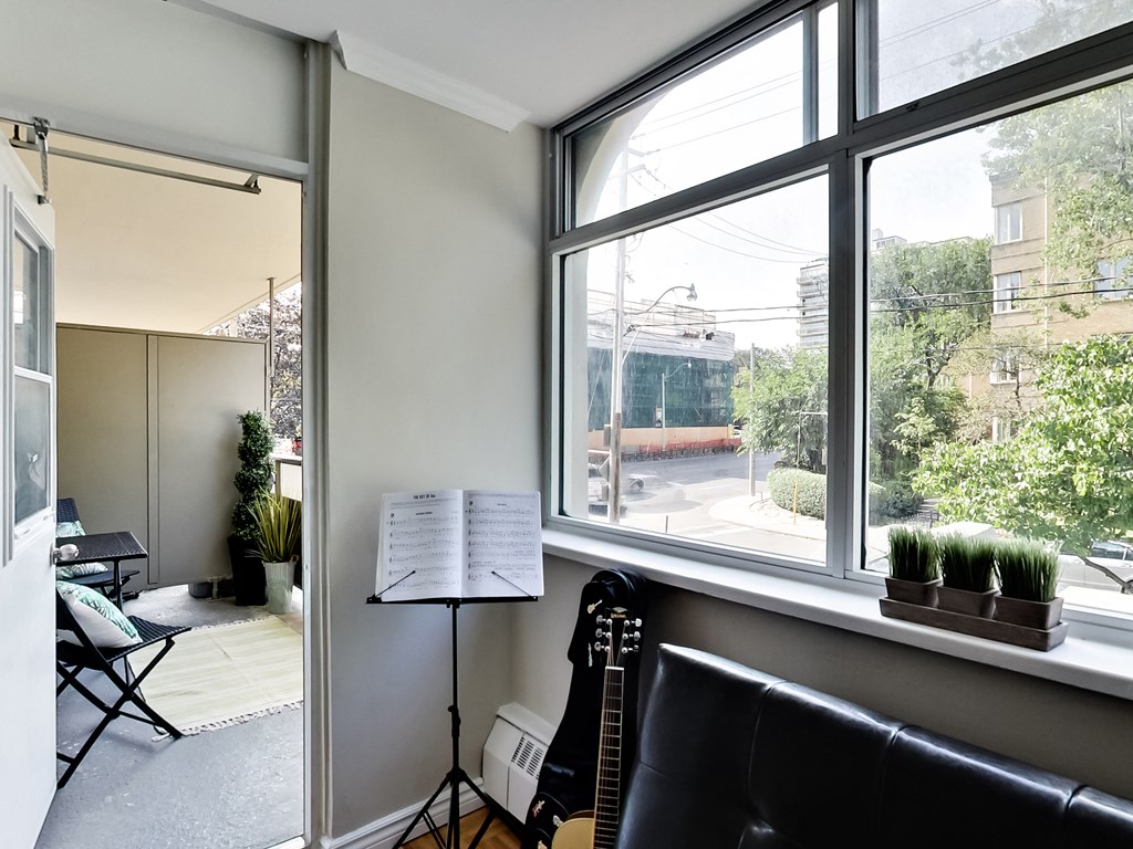 A room with a guitar, a chair, a music stand and a window.