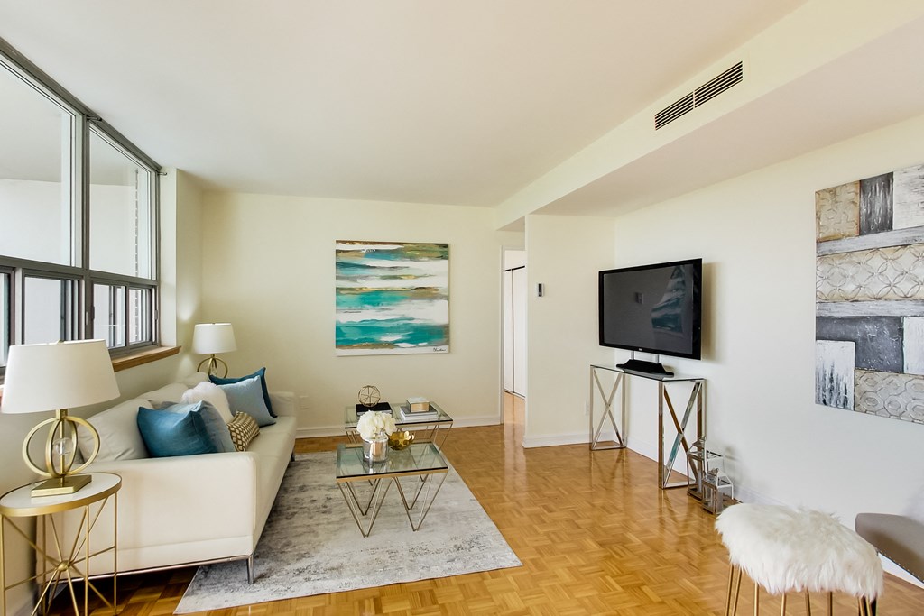 A living room with a white couch, a glass coffee table, and a television.