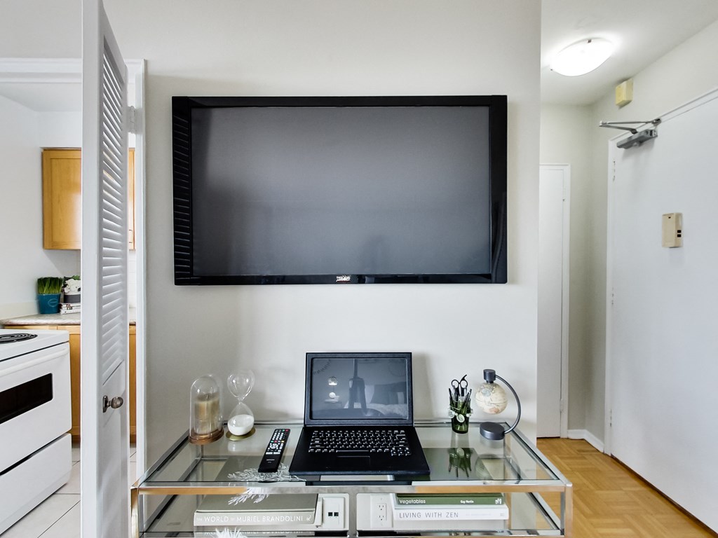 A black laptop is on a glass coffee table with a remote control and a book titled