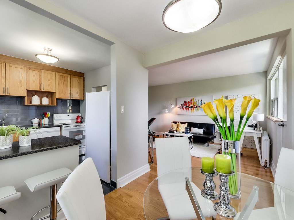 A kitchen with white chairs and a black counter top.