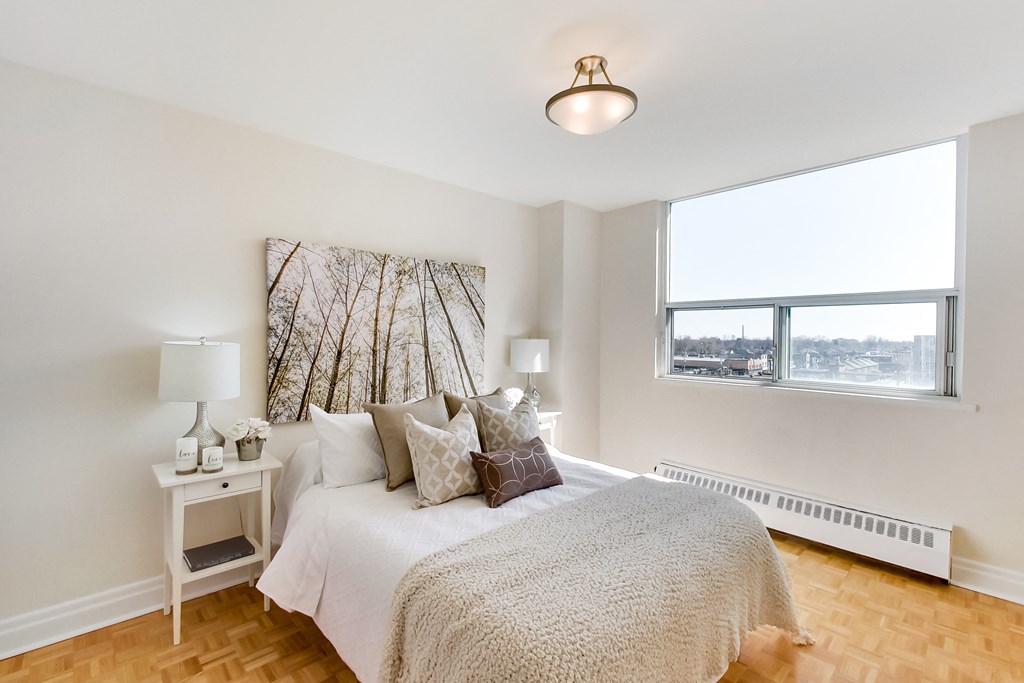 A bedroom with a large bed and a window overlooking a cityscape.