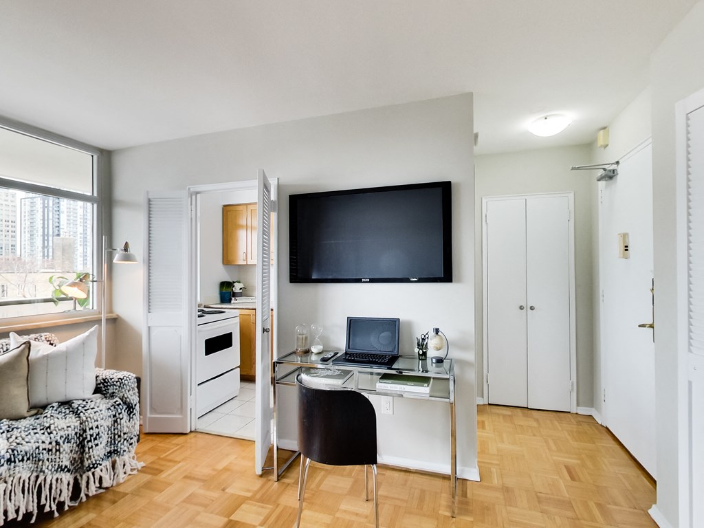 A room with a desk, chair, and a television mounted on the wall.