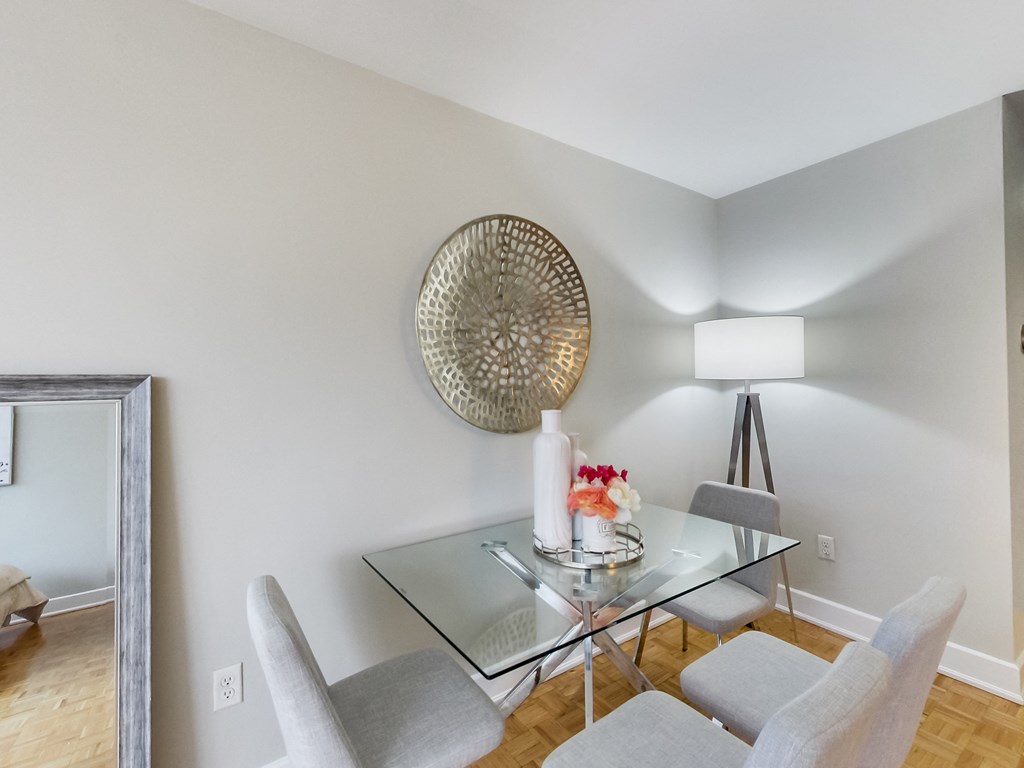 A dining room with a glass table and grey chairs.