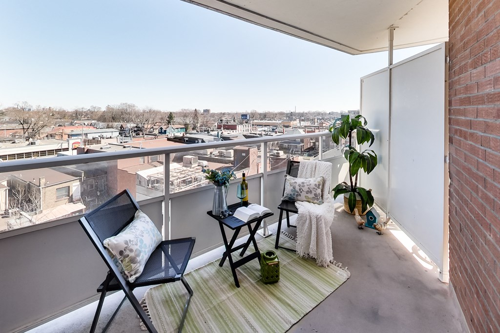 A balcony with a chair, table, and potted plant overlooking a cityscape.