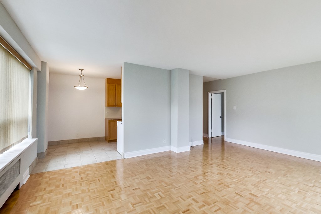 an empty living room with wood flooring and a door to a kitchen