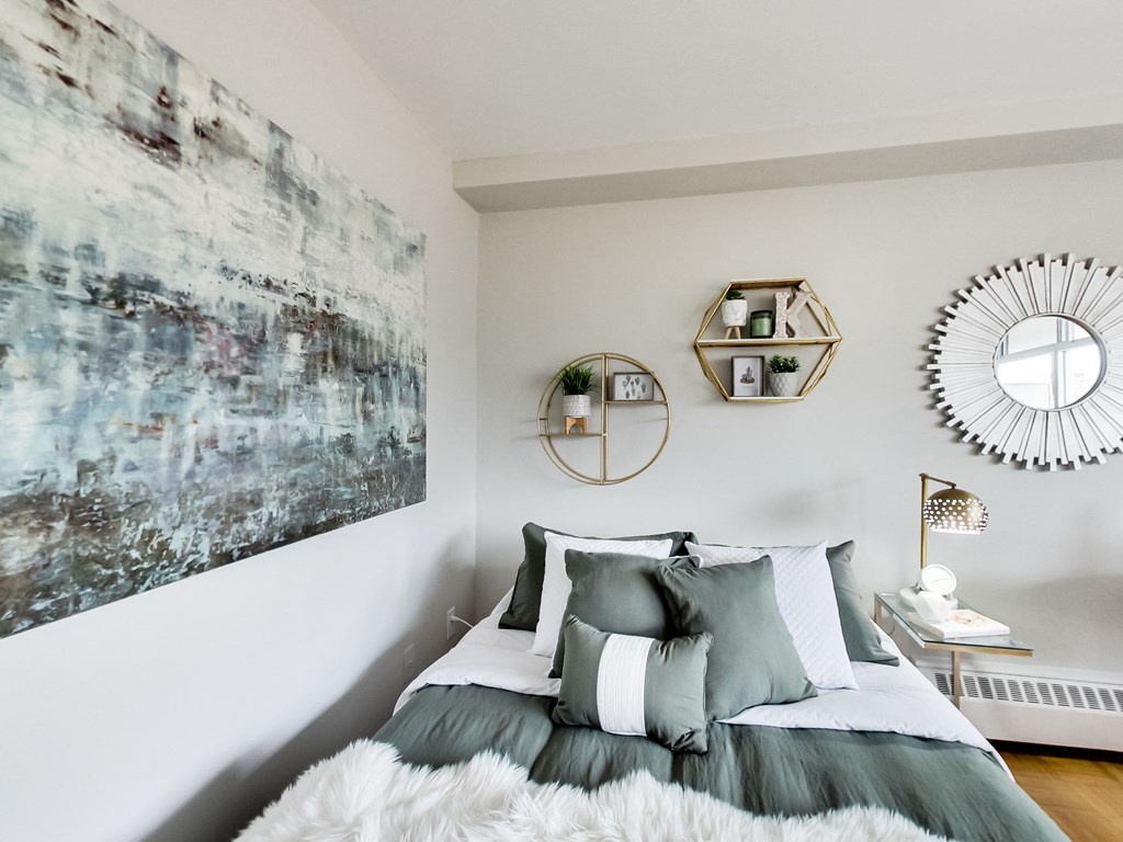 A bedroom with a large painting on the wall and a bed with a grey comforter.