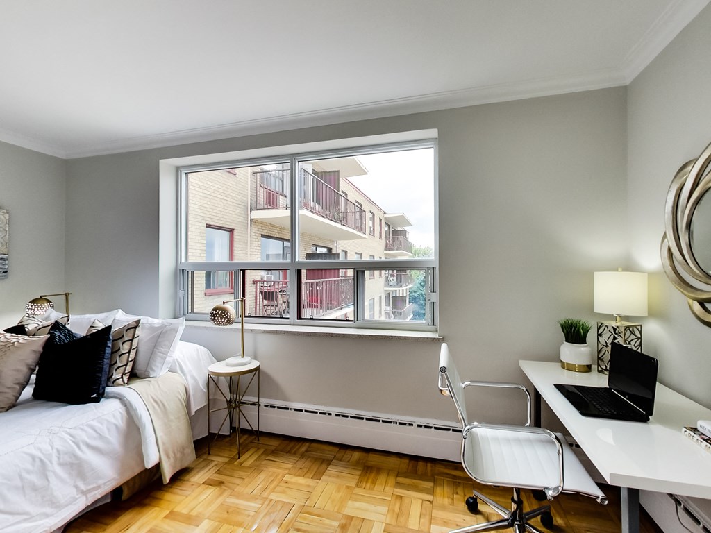 a bedroom with a large window and a bed and a desk with a laptop