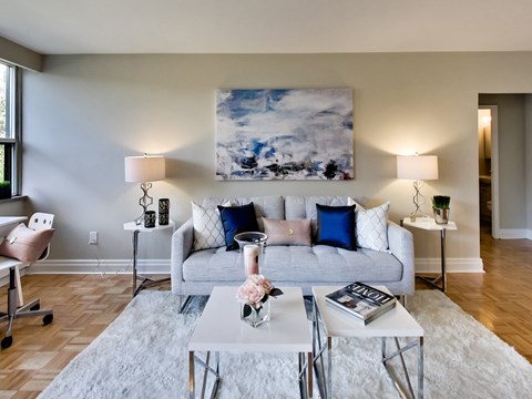 A living room with a grey couch, a white coffee table, and a painting on the wall.