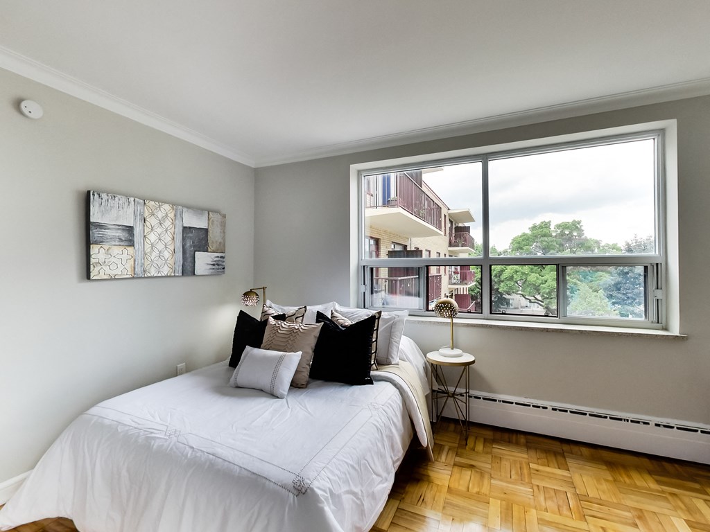 a bedroom with a large window and a bed with white sheets and pillows