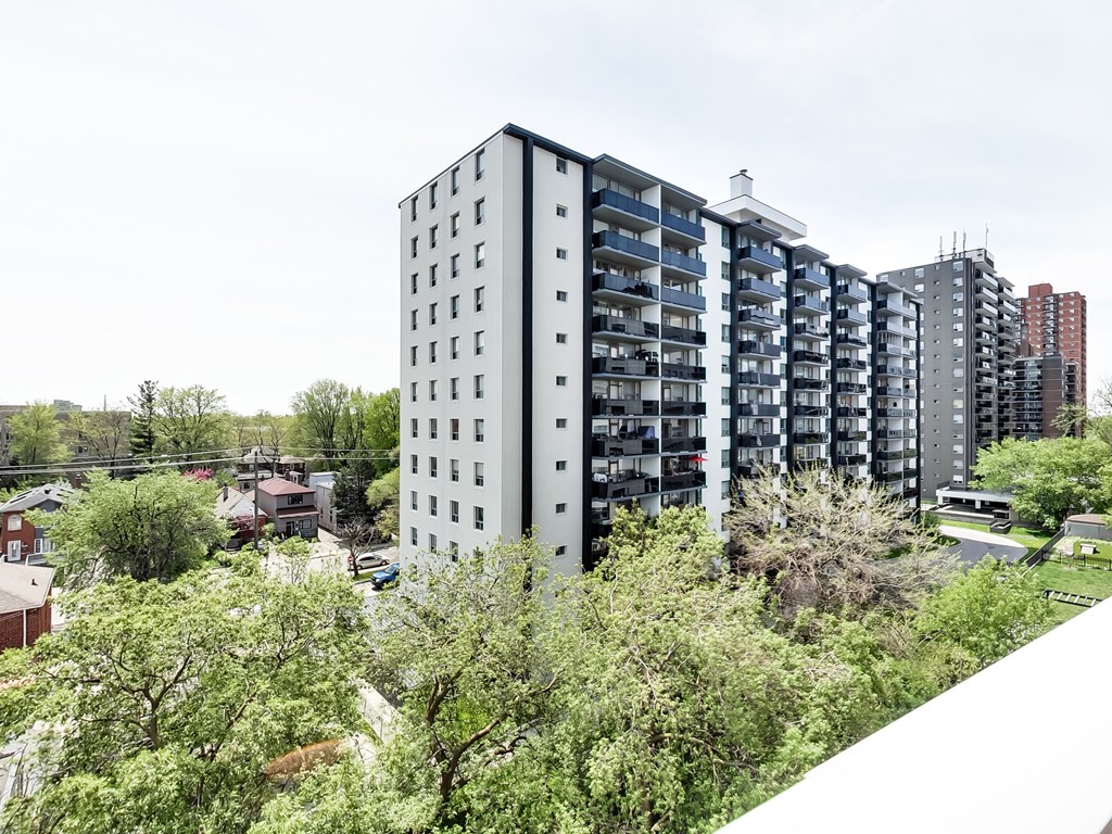 A tall residential building with balconies is surrounded by green trees.