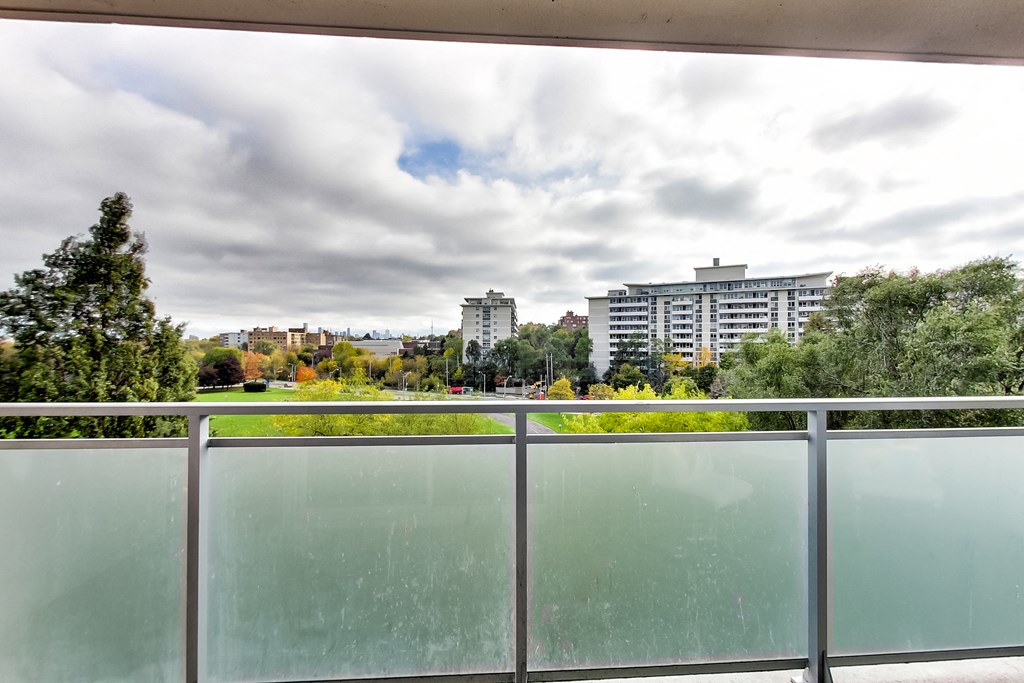 A view from a balcony looking out at a cityscape with buildings and trees.