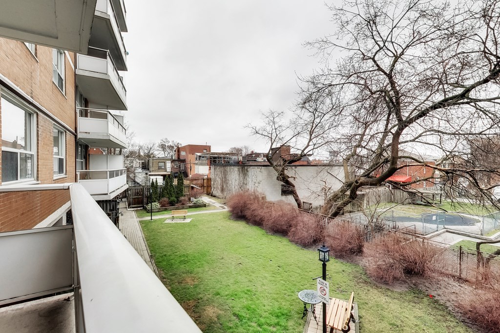 A balcony overlooks a green yard with a tree and a building in the background.
