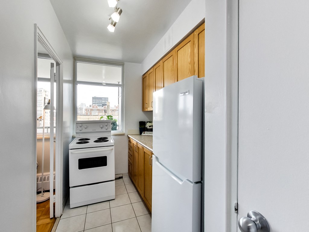A white refrigerator stands in a kitchen with wooden cabinets and a stove.