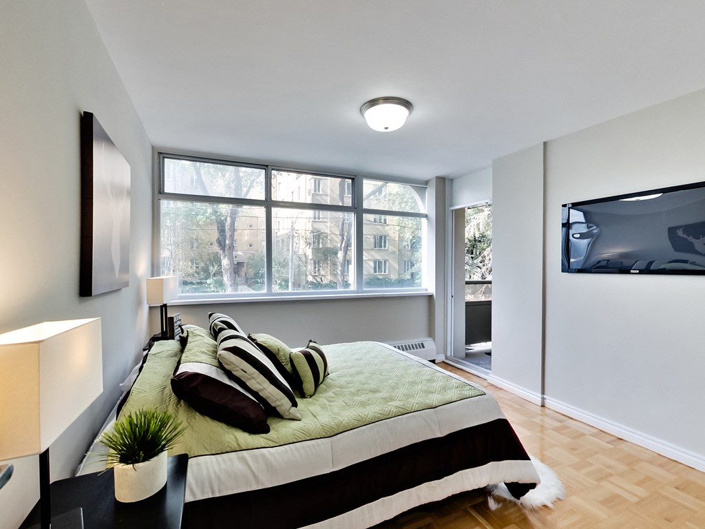 A bedroom with a bed, a chair, a lamp, and a window.