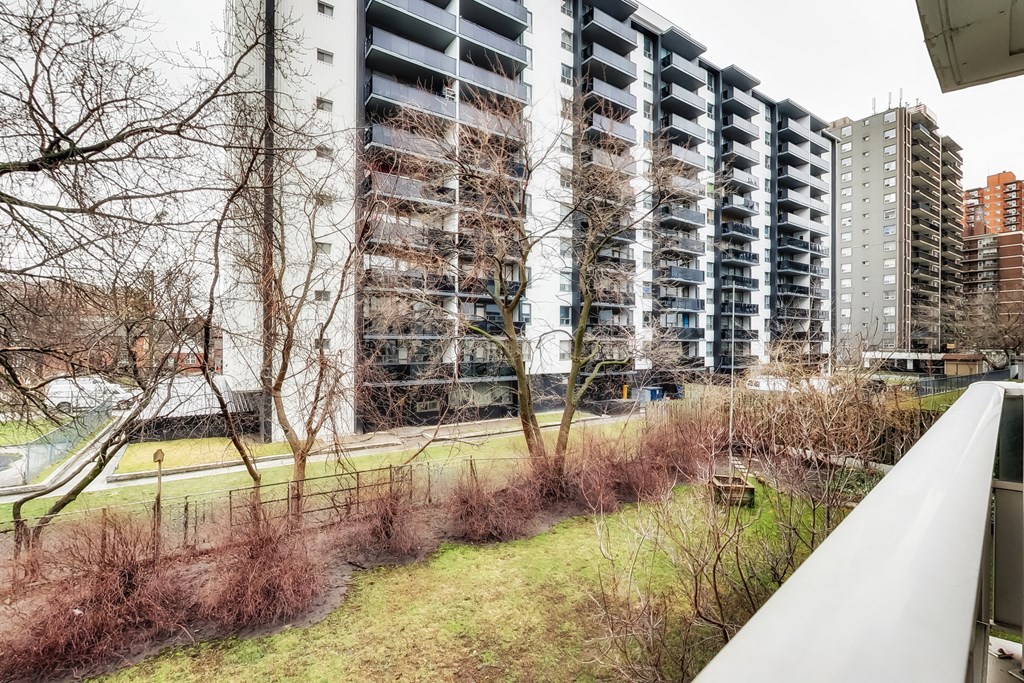 A tall residential building with balconies is surrounded by a grassy area and leafless trees.
