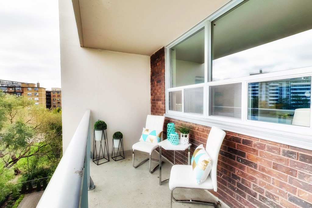 A balcony with a white chair and a small table with a plant on it.