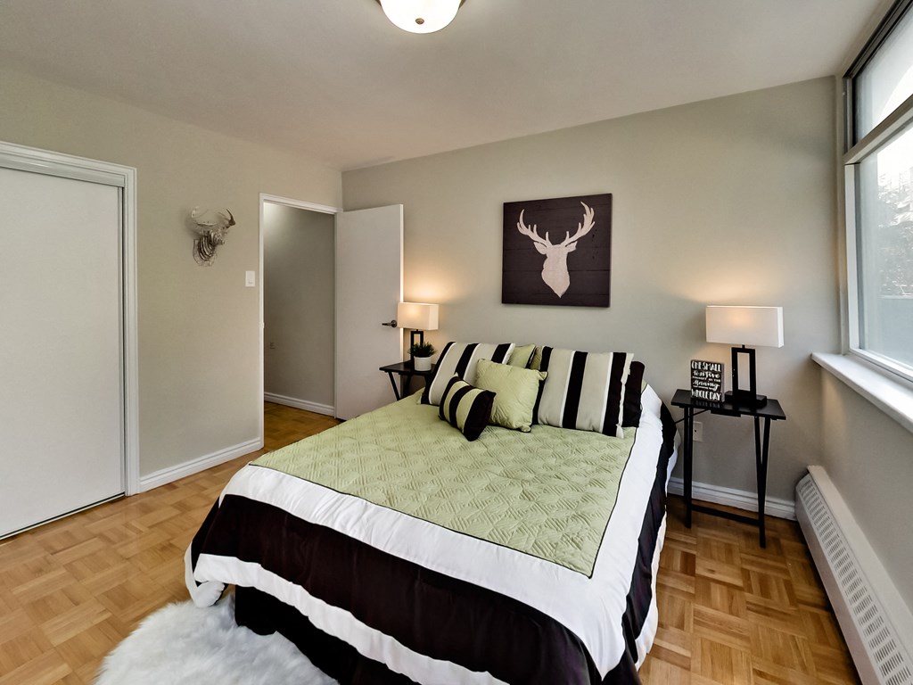 A bedroom with a bed, a nightstand, and a deer head picture on the wall.