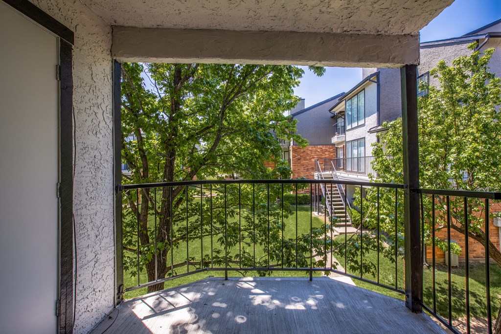 A balcony with a metal railing overlooks a green lawn and trees.