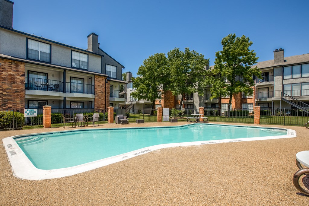 A swimming pool surrounded by a fence and chairs in front of a building.