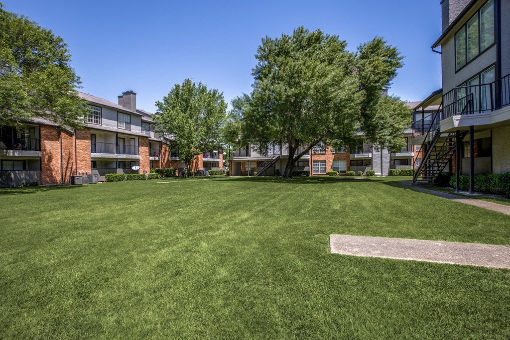 A large grassy area with trees and apartment buildings in the background.