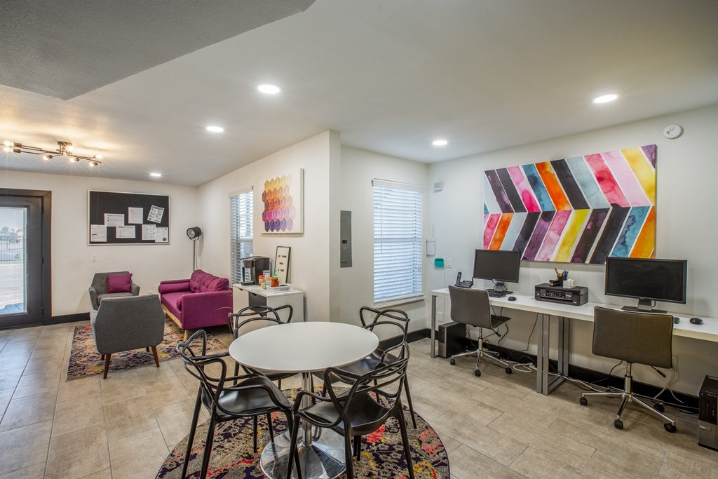 A room with a white table and chairs in the center with a computer desk and chairs to the right.