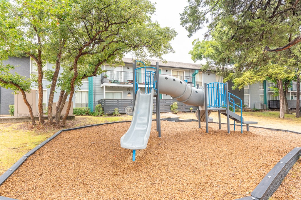 a playground with a slide and trees in front of a building
