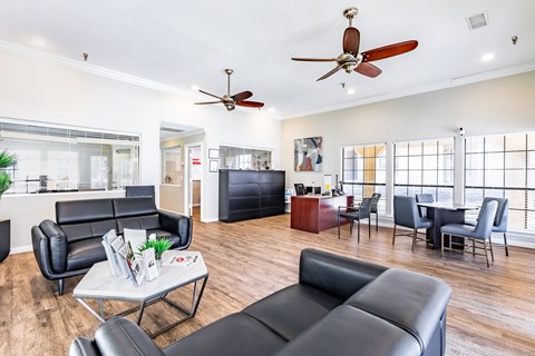A living room with black leather furniture and a ceiling fan.