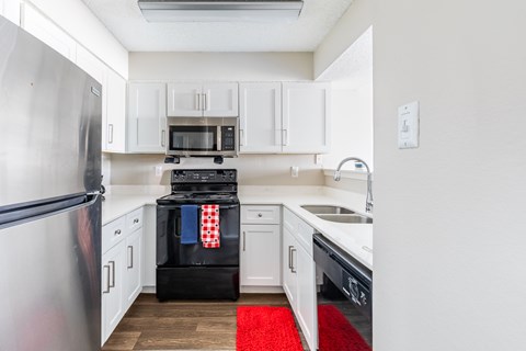 A kitchen with white cabinets and a red rug on the floor.
