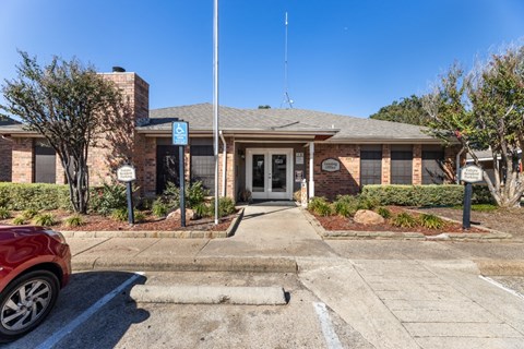 the front of a brick building with a driveway and a car parked in front