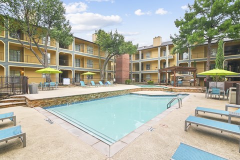 A swimming pool surrounded by apartment buildings and lounge chairs.