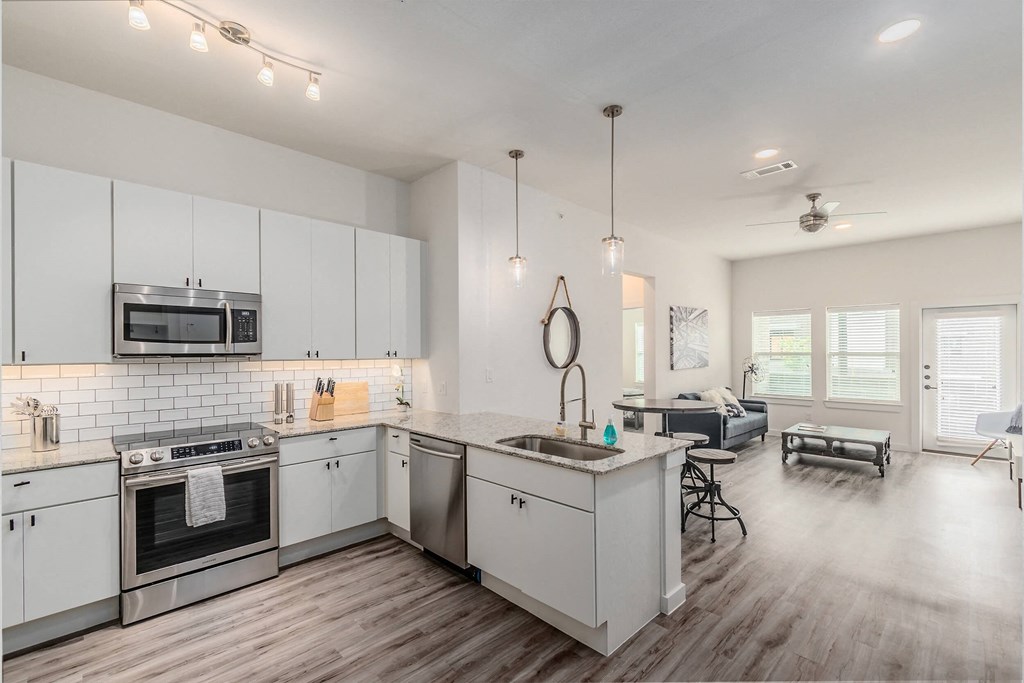 an open kitchen and living room with white cabinets and stainless steel appliances