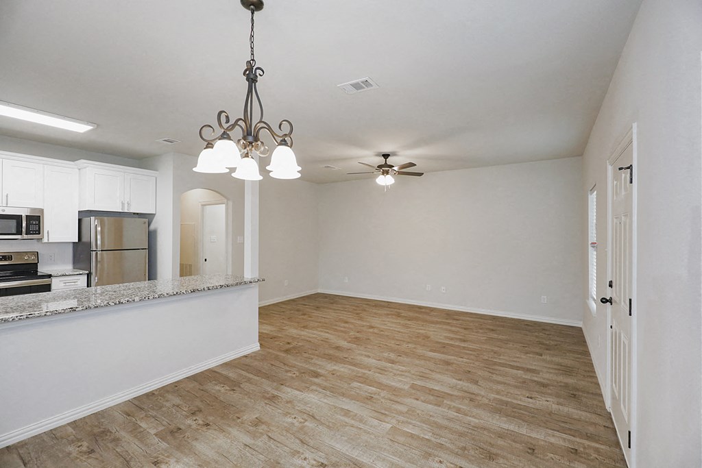 an empty living room with a kitchen and a ceiling fan