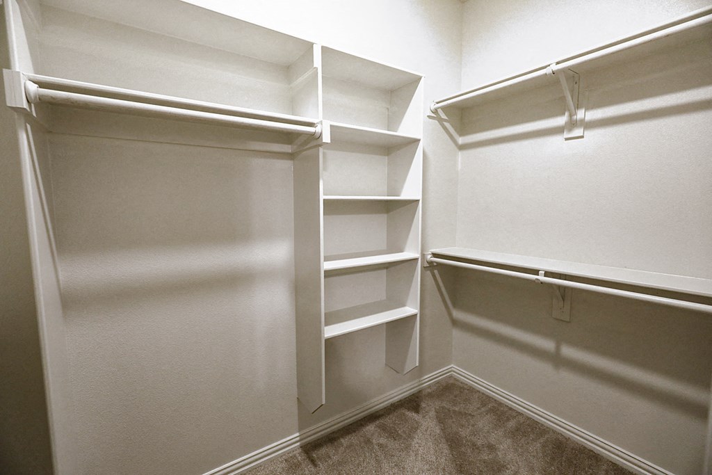 a walk in closet in a home with white walls and shelves