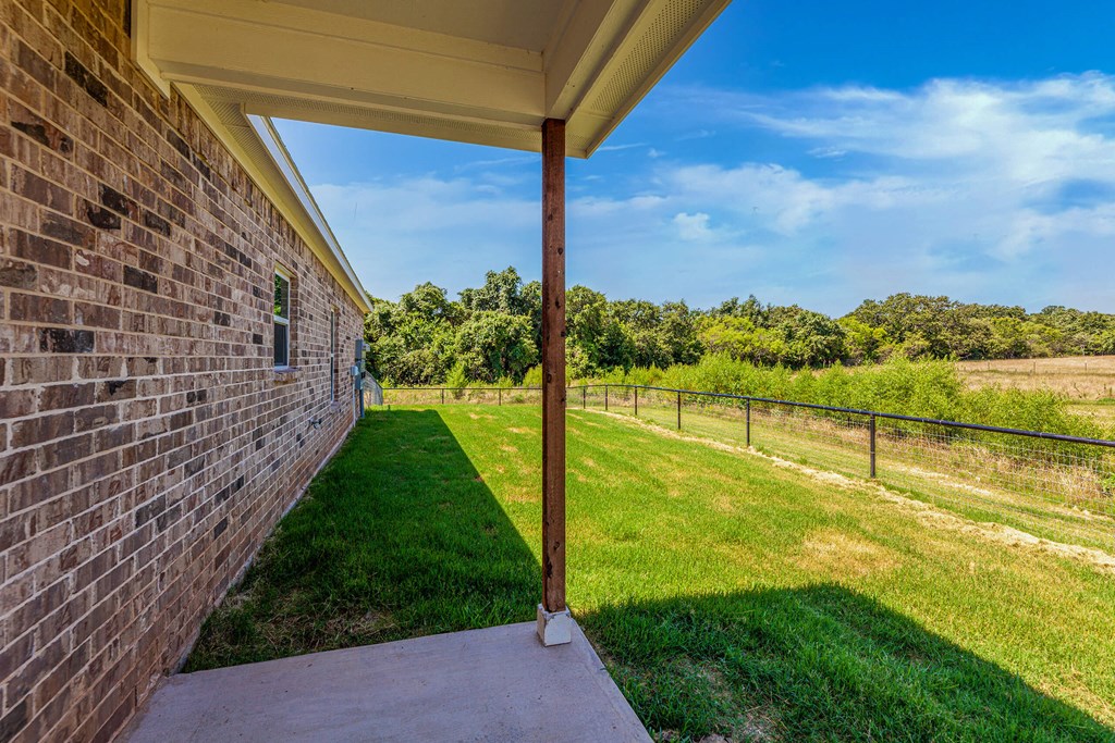 the back porch of a brick house with a yard and a fence