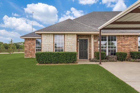 the front of a brick house with a driveway and grass
