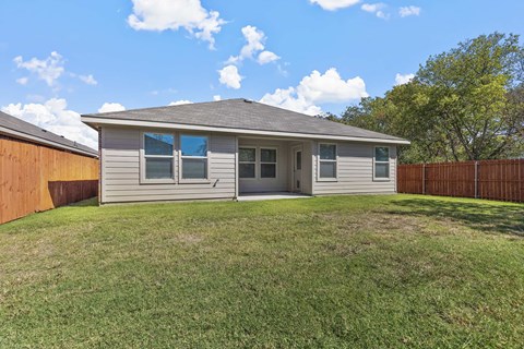 a small gray house with a yard and a wooden fence