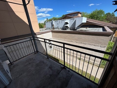 A balcony with a black railing and a view of a house and trees.