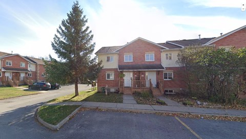 the front yard of a brick house with a sidewalk and a tree
