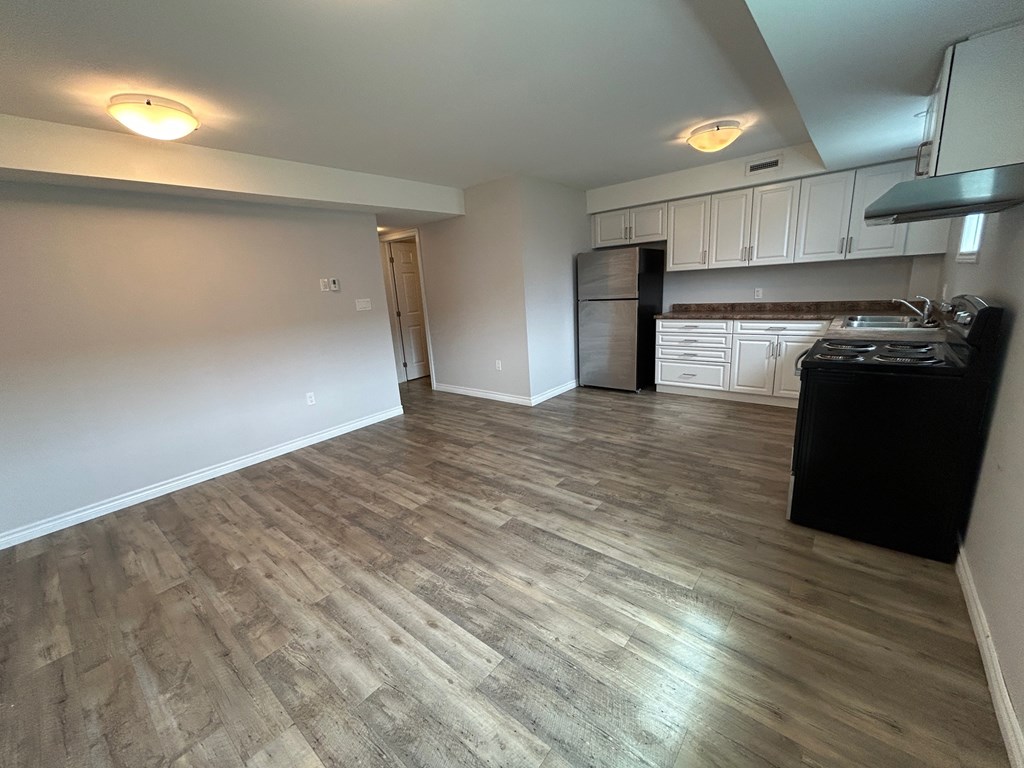 A kitchen with a black refrigerator and wooden flooring.